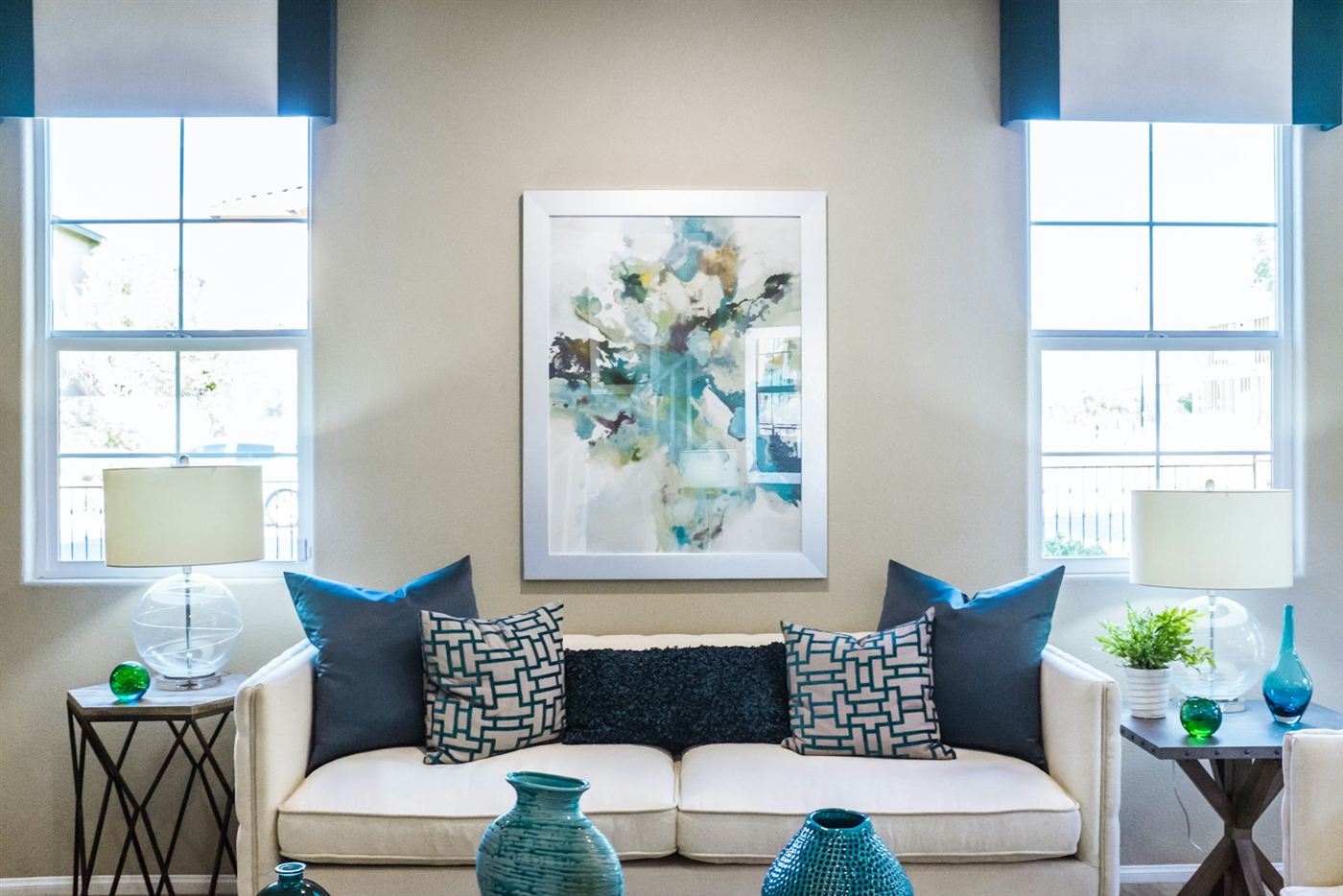 Woonkamer met witte bank, blauwe kussens en twee hoge ramen